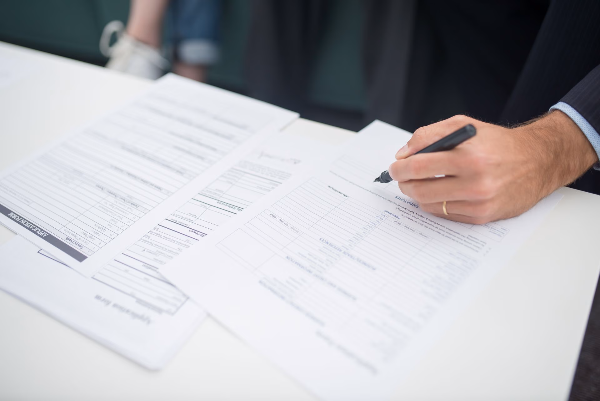 Person wearing a suit fills out a job application form with a pen on a white desk.